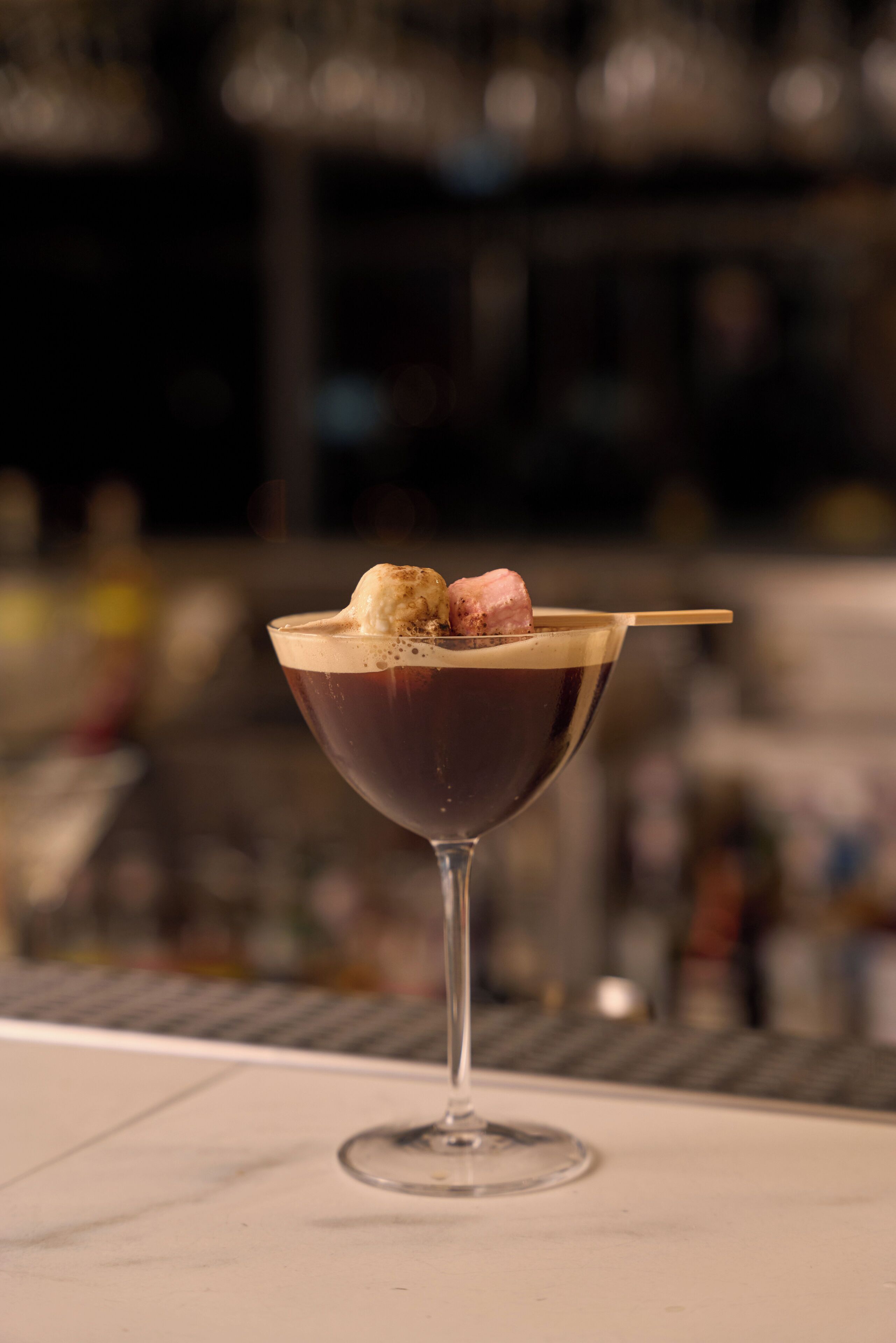 A cocktail with a chocolate sphere and a straw, served in a martini glass.