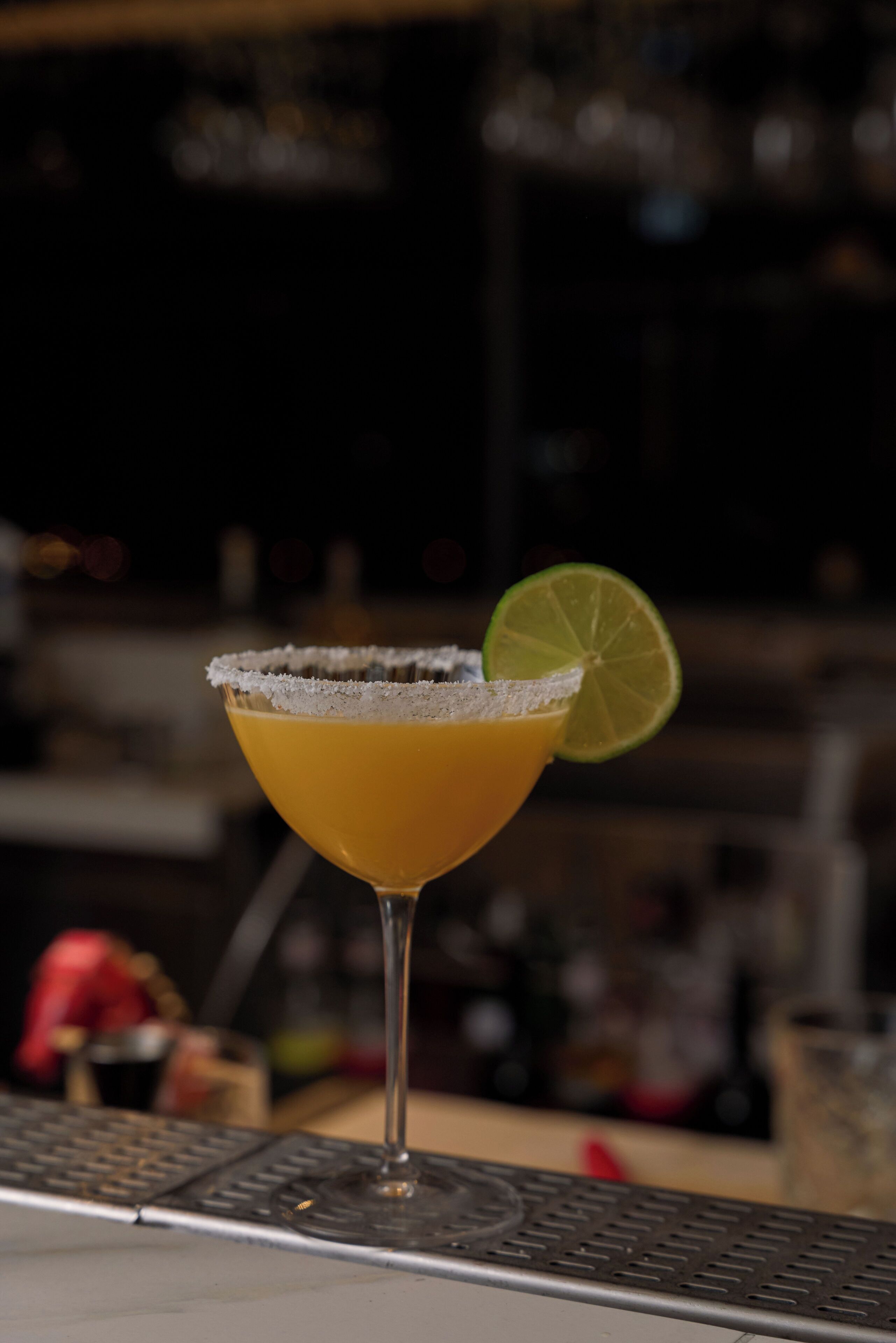 A cocktail with a salted rim and a lime garnish on a bar counter.