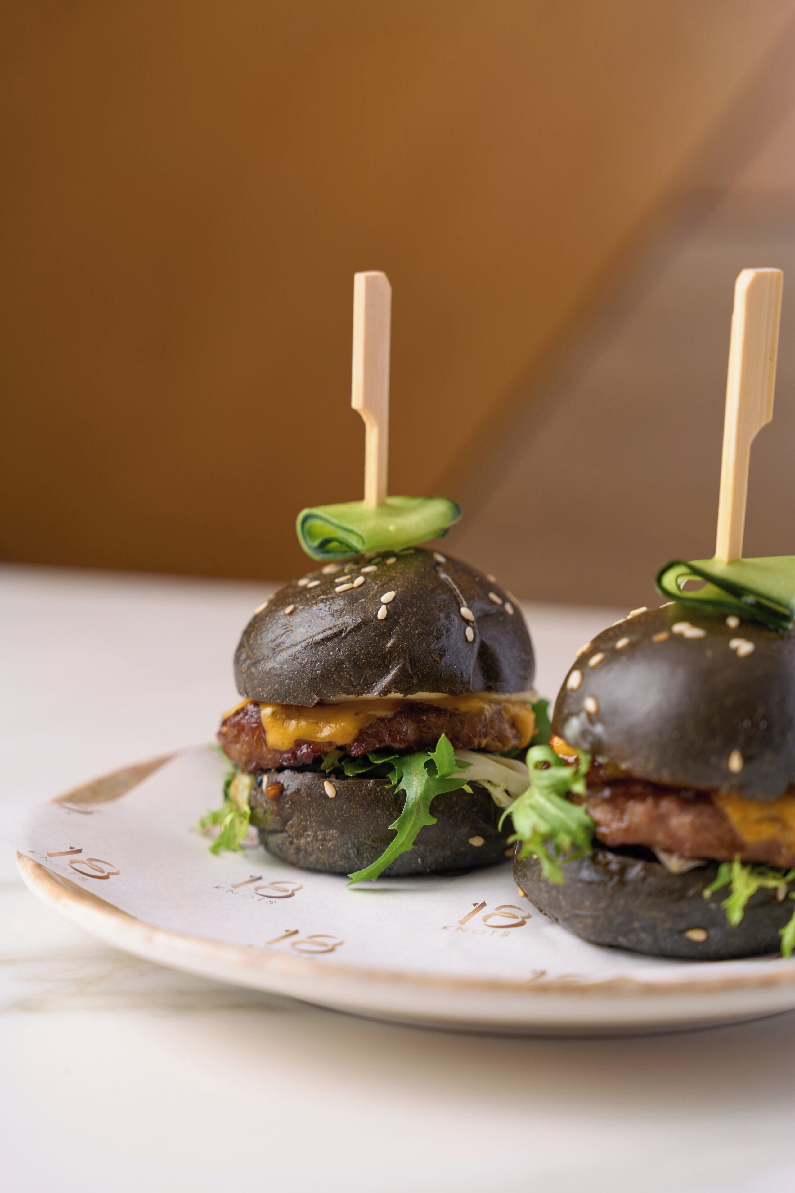 Dos hamburguesas con semillas de sésamo sobre un plato con el número 18.