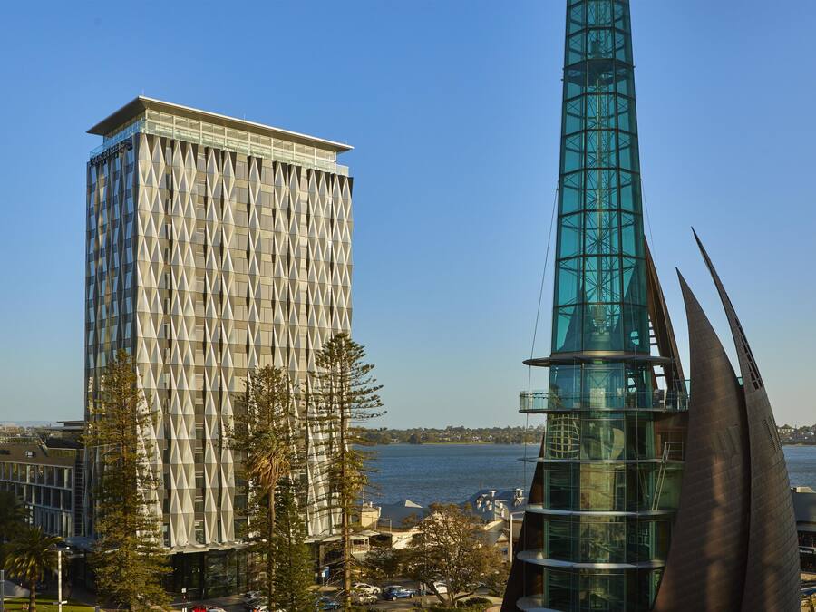 A modern building with a glass facade and a unique geometric design, situated near a body of water.