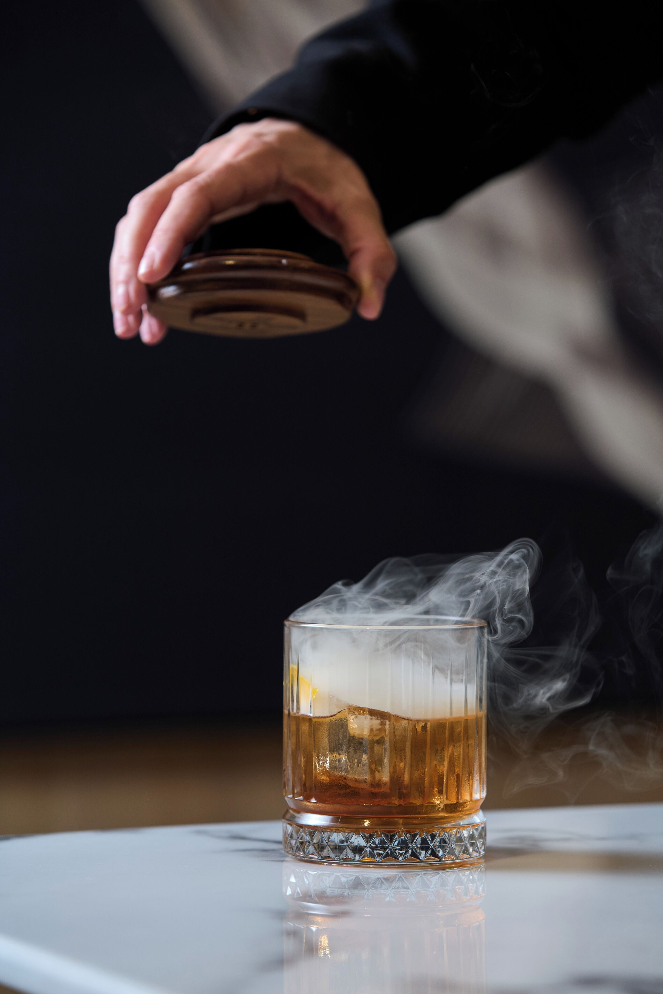 A hand pouring a drink into a glass with smoke rising from it.