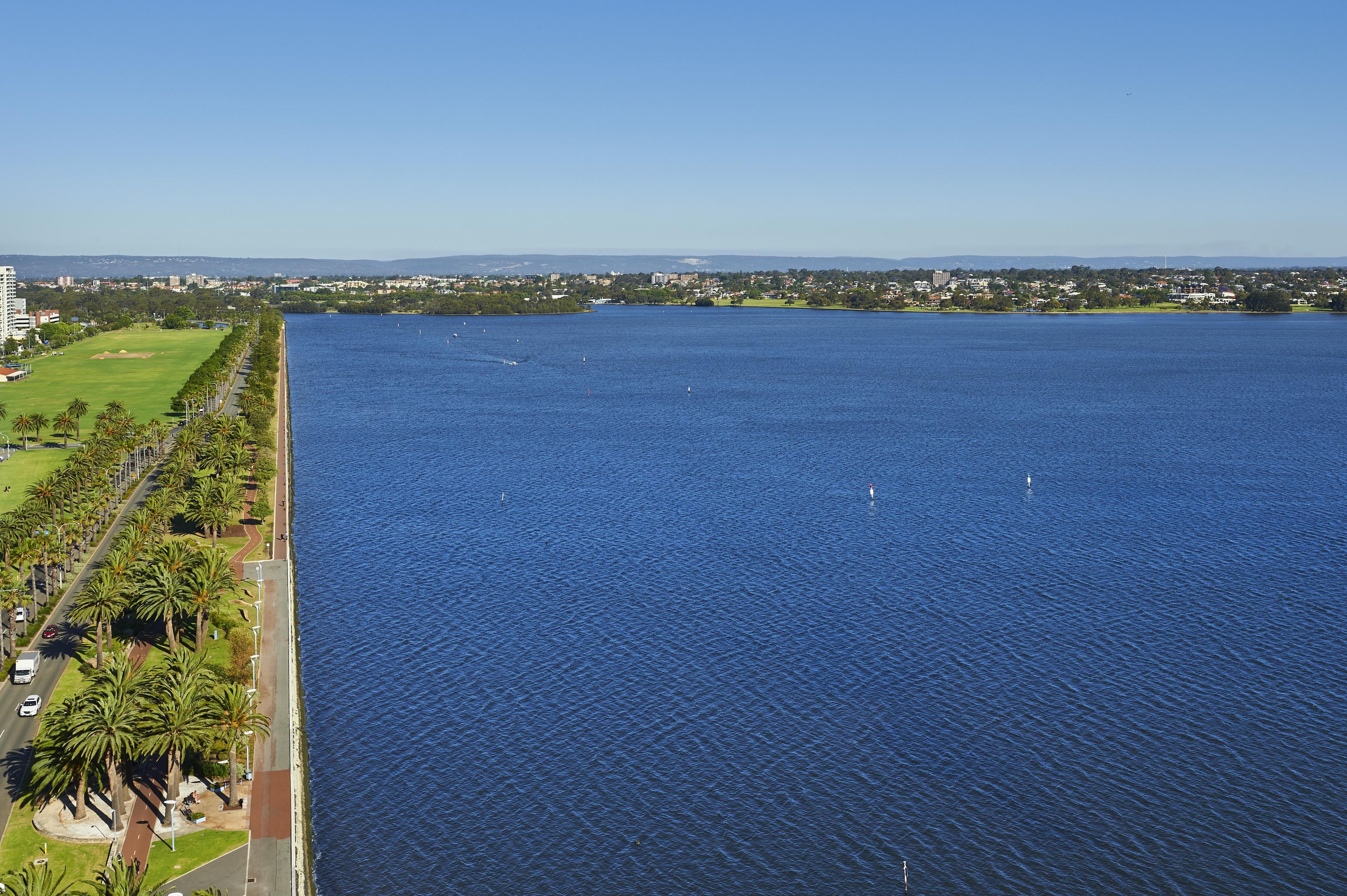 A large body of water with a road running alongside it, bordered by greenery and buildings in the distance.