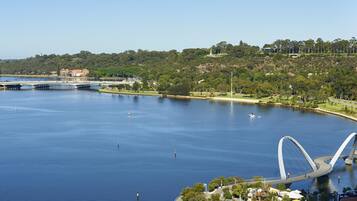 A large body of water with a modern bridge, a park with trees, and buildings in the background.
