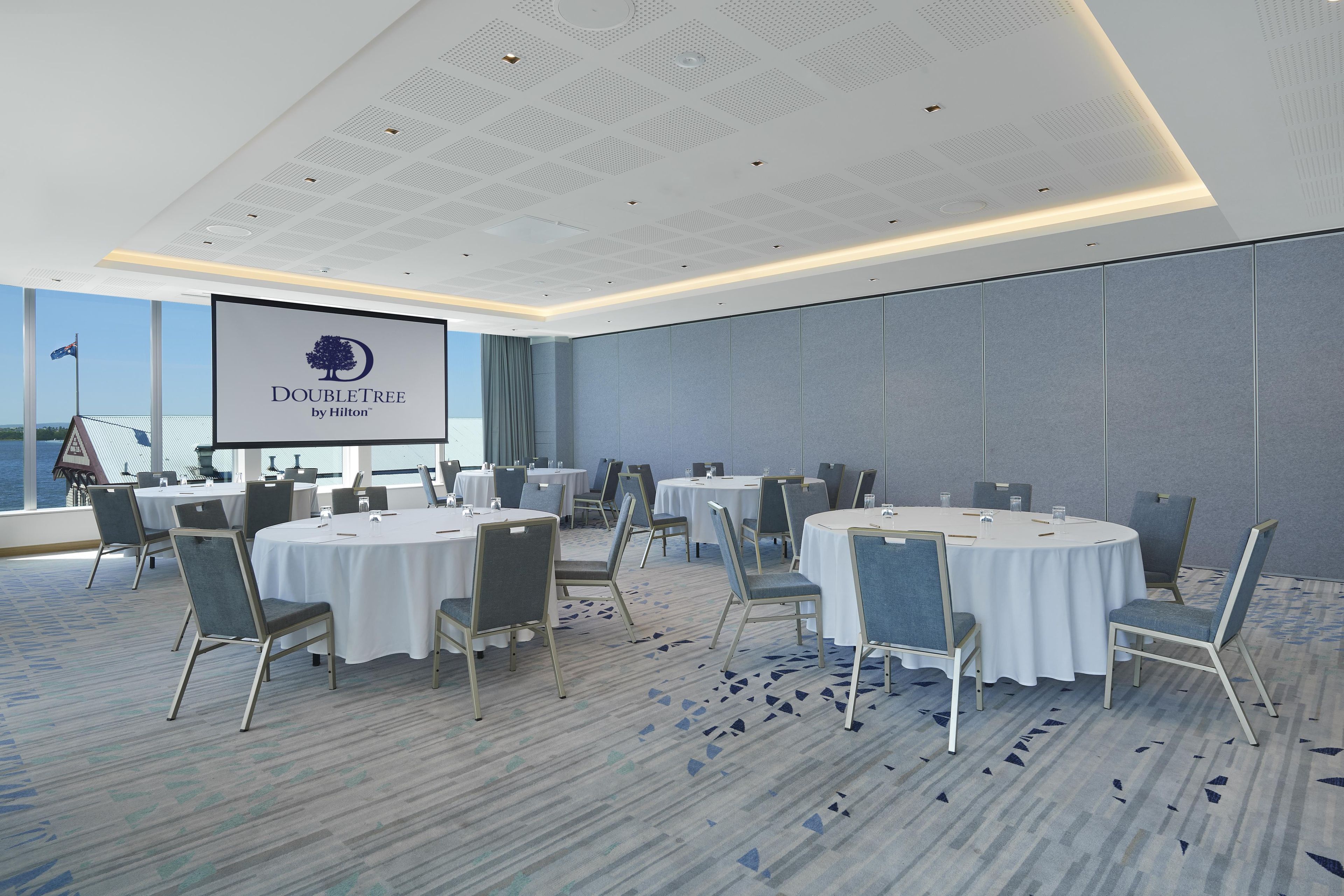 A conference room with round tables, chairs, and a large screen displaying the DoubleTree by Hilton logo.