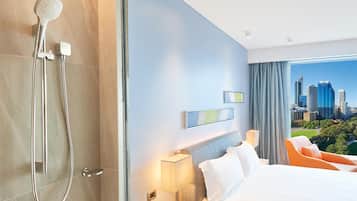 Quarto de hotel moderno com uma cama grande, mesa de cabeceira com abajur, chuveiro e vista para a cidade.