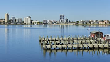 A waterfront cityscape with a dock and a small building, likely a marina or boathouse, with a clear view of the city skyline in the background.