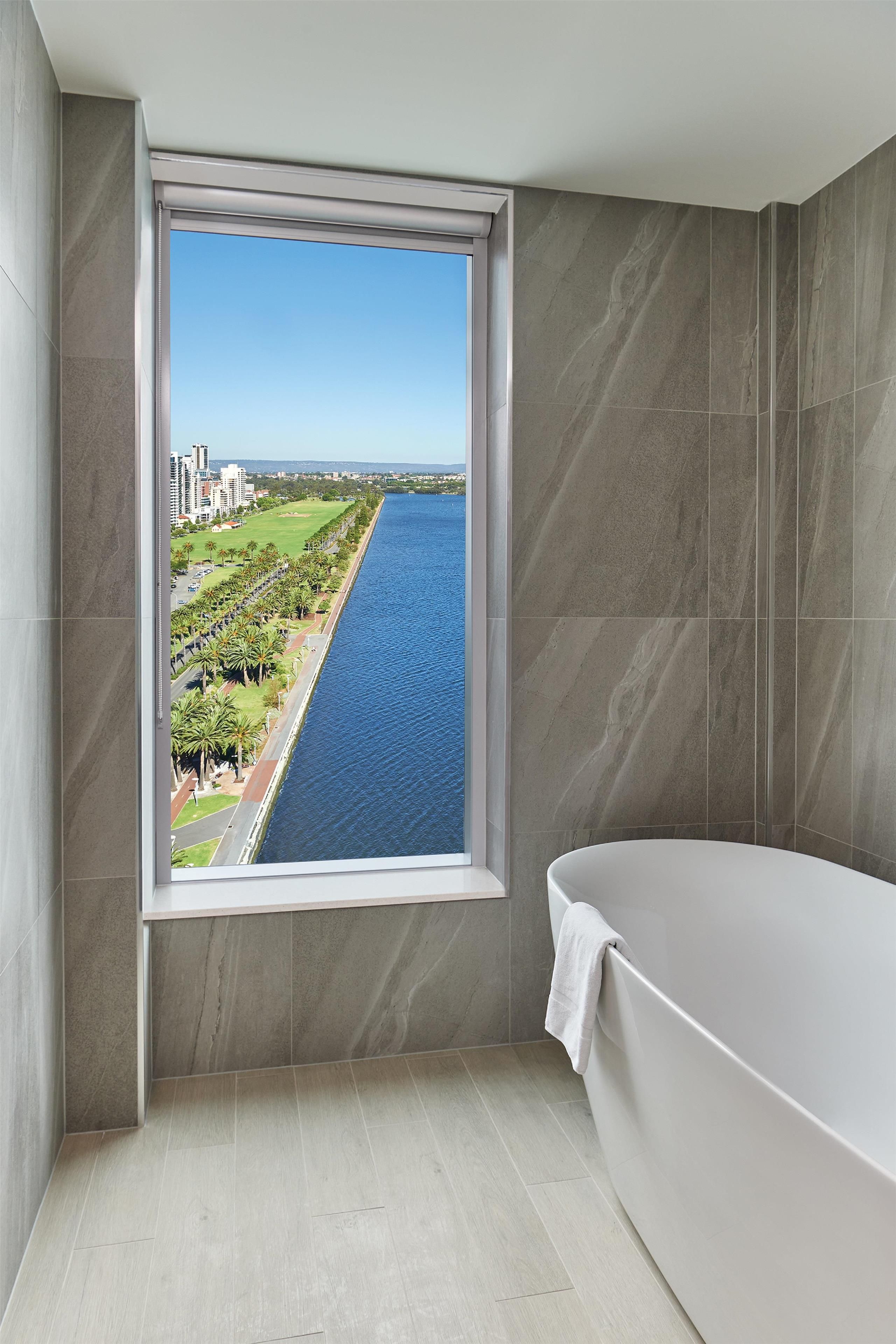A bathroom with a large window offering a view of a river and cityscape.