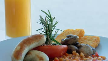 Un plato de comida con salchichas, frijoles y tomate, con un vaso de jugo de naranja al fondo.