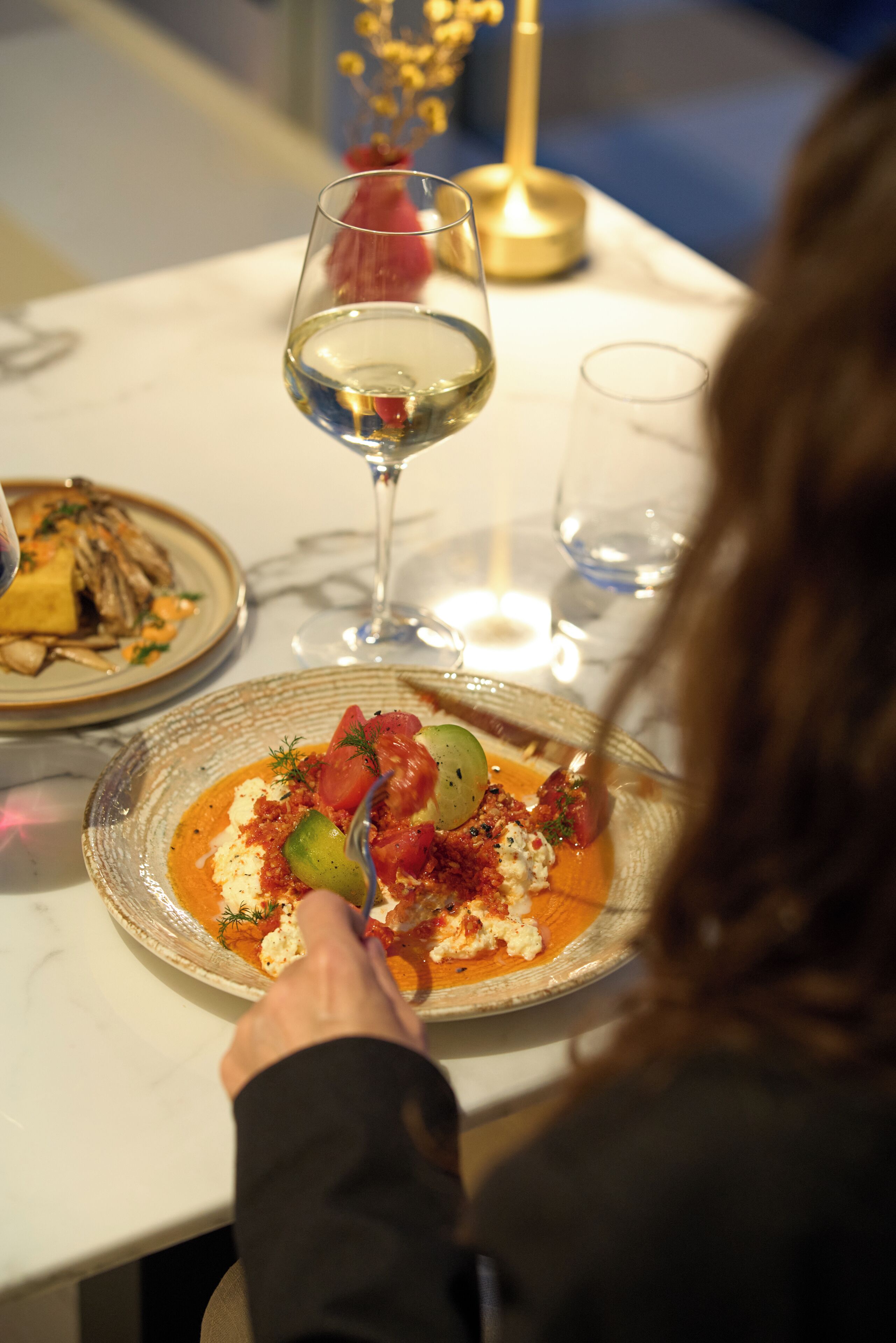 A dining table with a plate of food, a wine glass, and a candle.