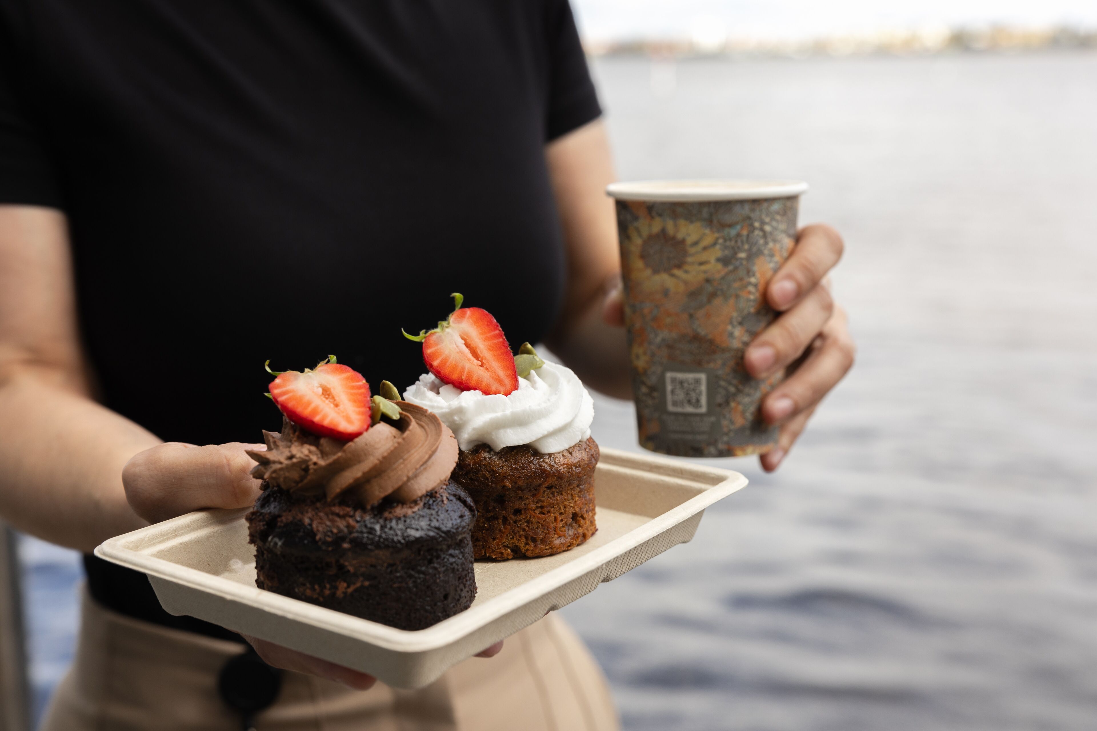 Una persona che tiene un vassoio con due cupcake e una tazza di caffè.