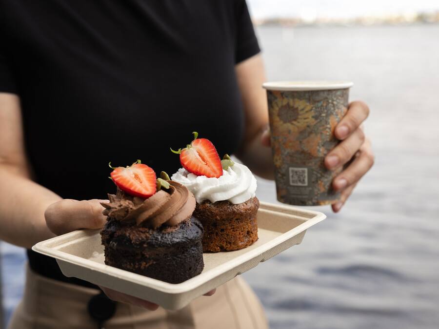 Una persona che tiene un vassoio con due cupcake e una tazza di caffè.