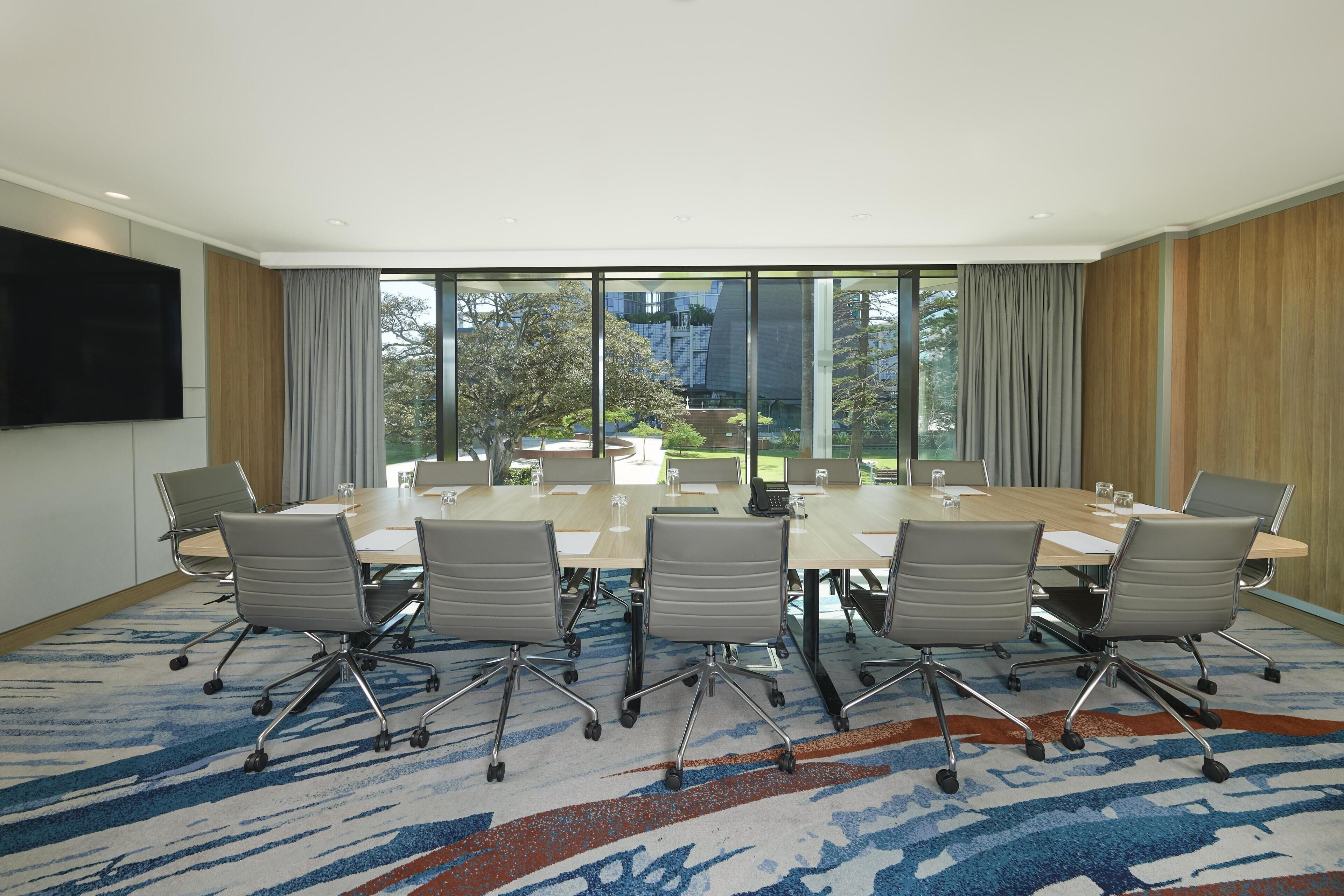 A conference room with a large table, six chairs, and a TV on the wall.