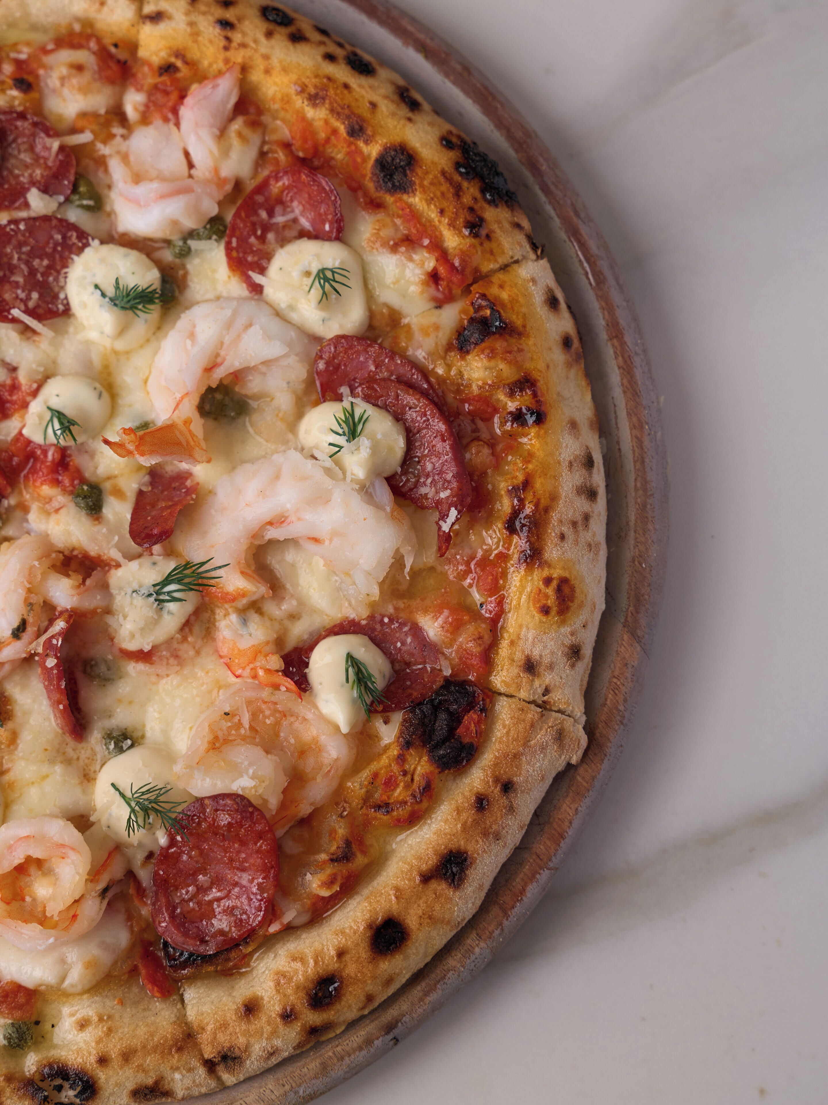 Pizza met garnalen, worst en kaas op een houten plank.