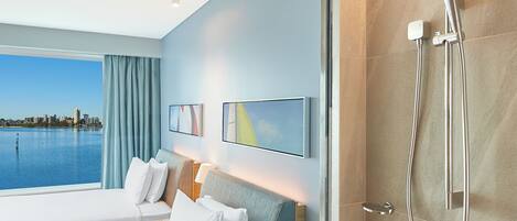A hotel room with a large bed, a shower, a city view, and a modern design.