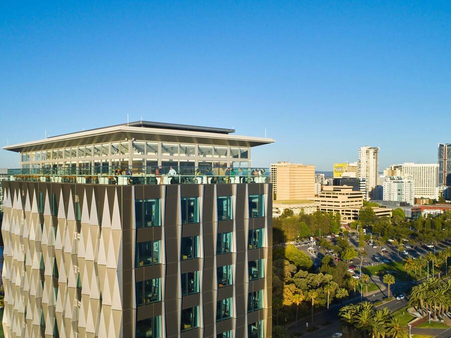 A modern high-rise building with a glass facade, multiple floors, and a rooftop terrace.
