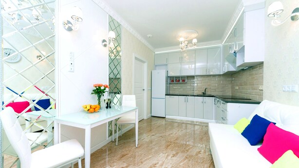 A modern kitchen with white cabinets, a dining area with a glass table, and a living area with a white sofa. - Comfortable apartment in a new house (Kyiv)