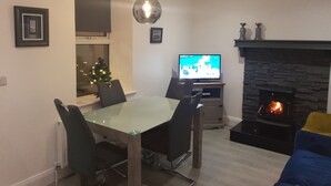 En moderne stue med et glasbord, sorte stole, et fladskærms-tv, en pejs og et lille juletræ.