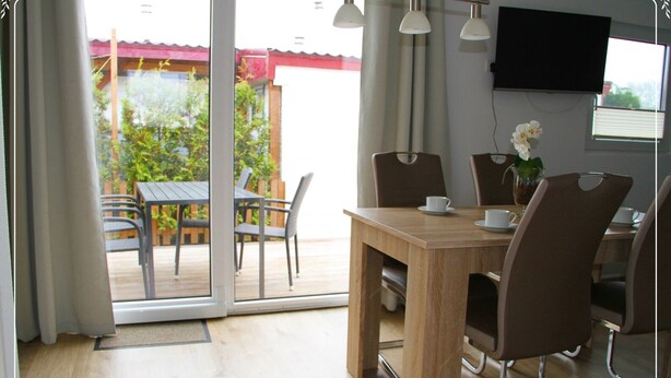 A dining area with a wooden table and chairs, a TV mounted on the wall, and a view of the outdoor patio. - Holiday home De Wickinger with your own Steiger angler are welcome! (Wervershoof)
