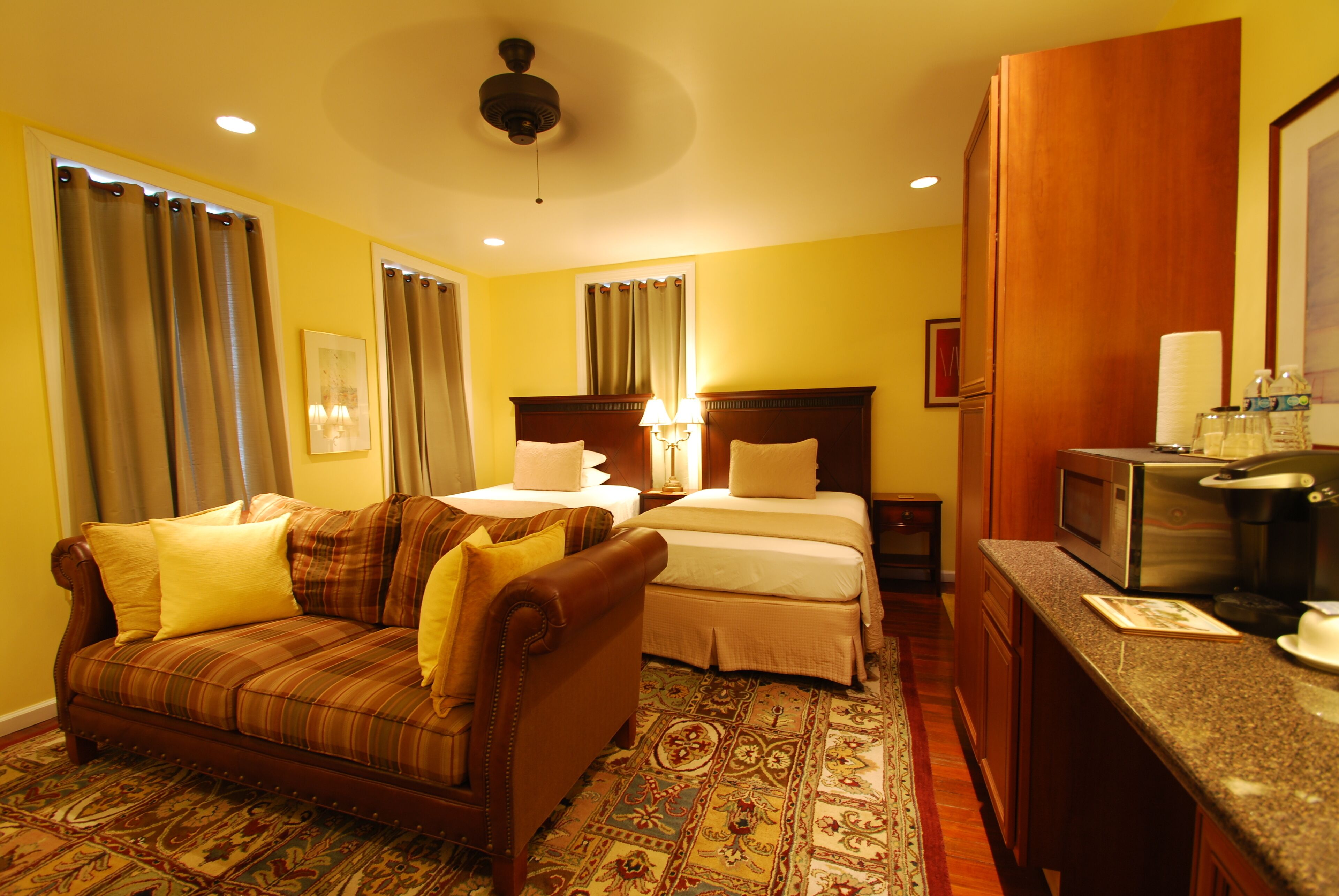 A hotel room with a bed, a sofa, a desk with a microwave, and a bathroom with a sink and mirror.