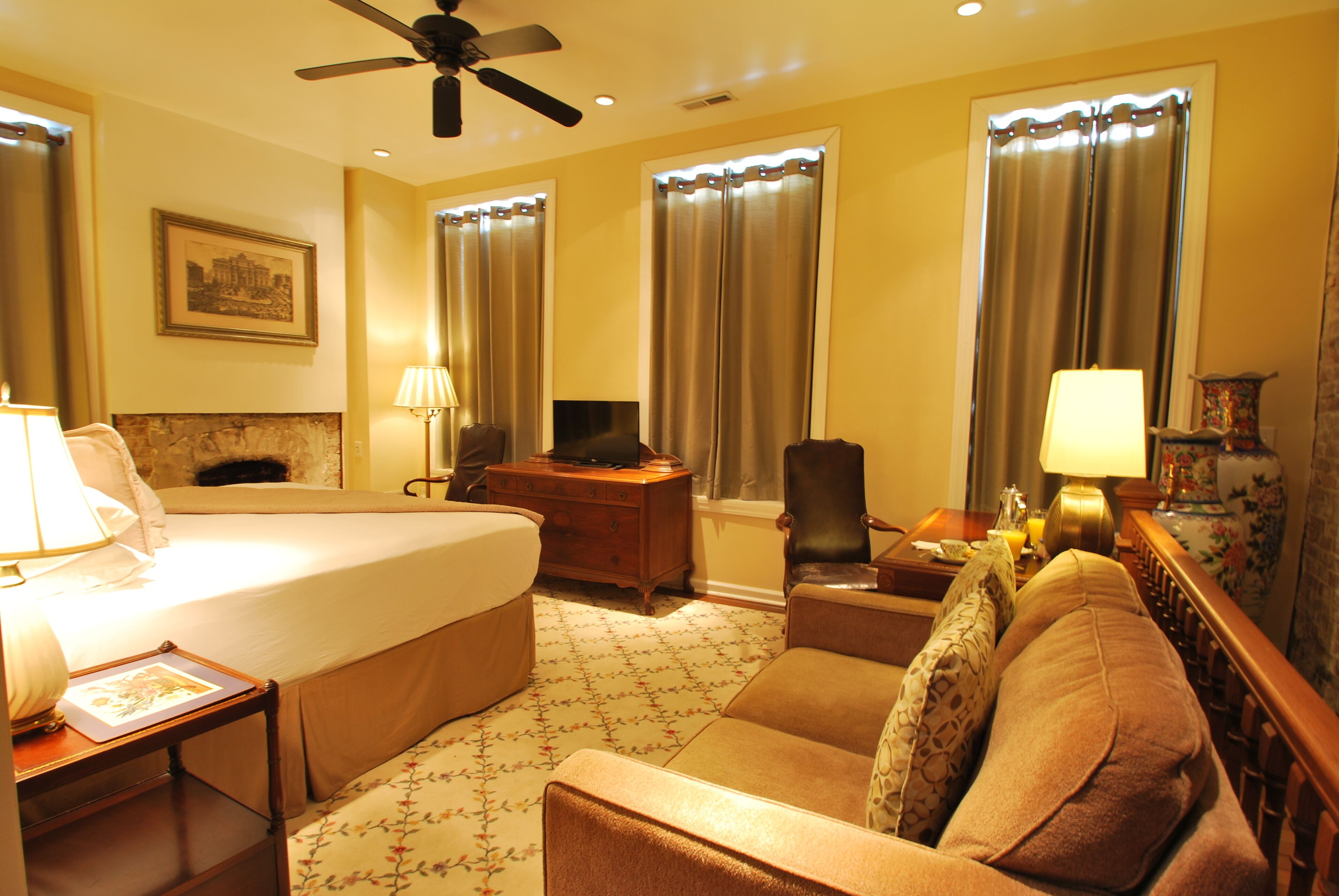 A hotel room with a bed, a desk, a chair, a sofa, and a ceiling fan.