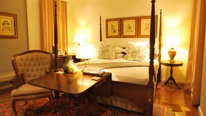 Ein Hotelzimmer mit einem Himmelbett, einem Esstisch mit Stühlen, einem Nachttisch mit Lampen und einem Teppich mit Blumenmuster.