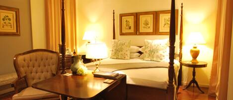 A hotel room with a four-poster bed, a dining table with chairs, a bedside table with lamps, and a floral-patterned rug.