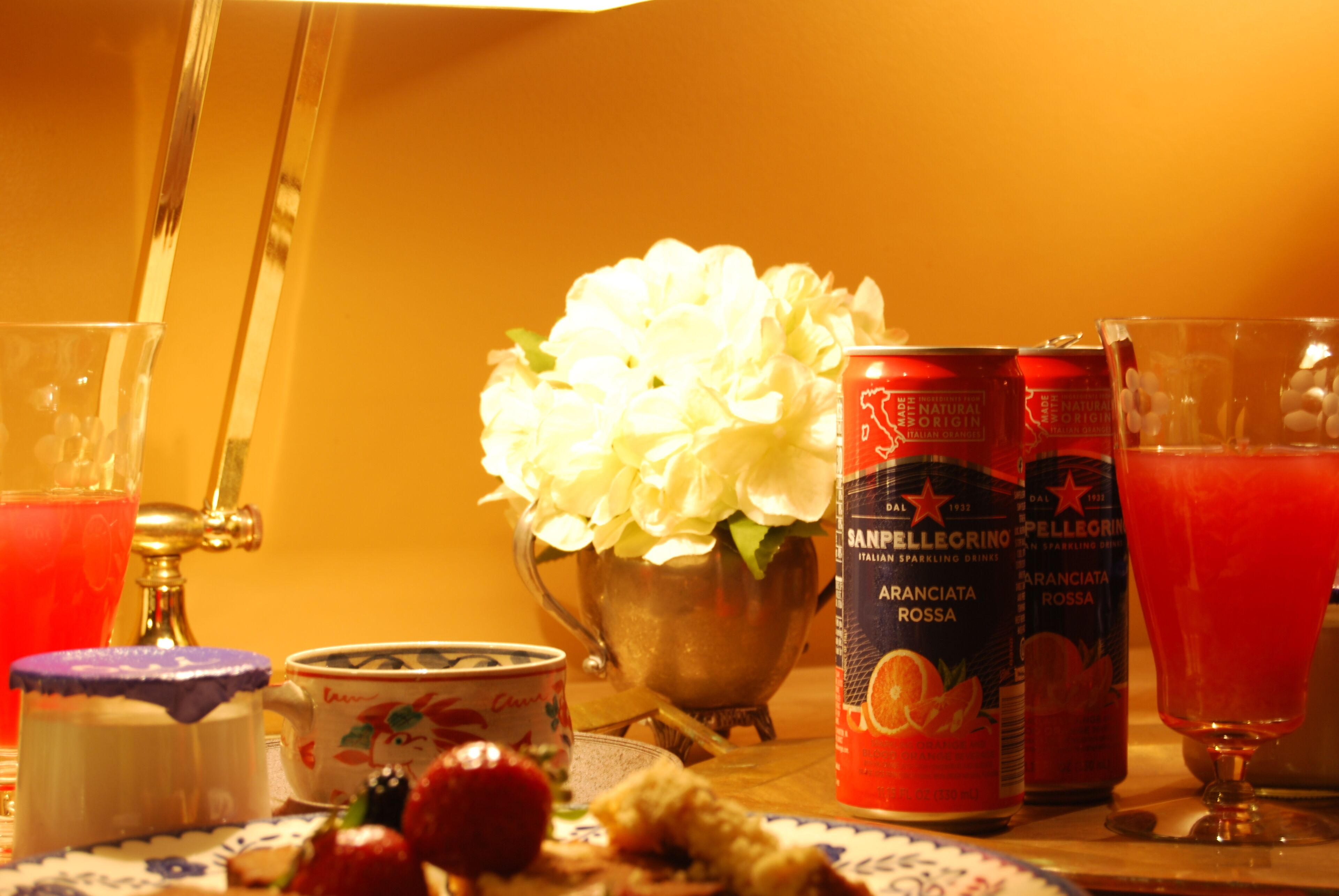 Ein Tisch mit einer Blumenanordnung, einer San Pellegrino-Wasserflasche, einem Glas roter Saft und einem Teller mit Speisen und einer Tasse.