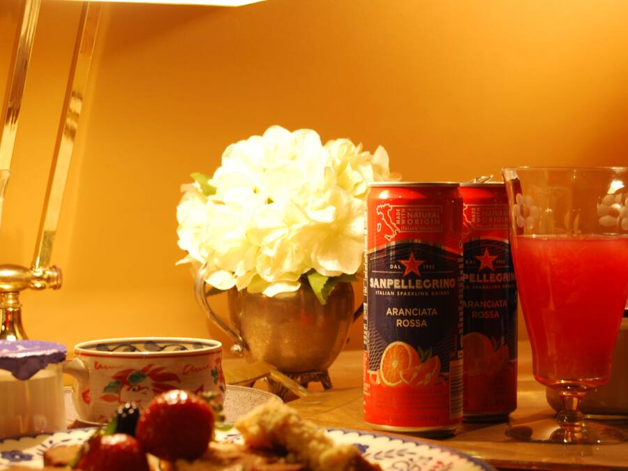 Ein Tisch mit einer Blumenanordnung, einer San Pellegrino-Wasserflasche, einem Glas roter Saft und einem Teller mit Speisen und einer Tasse.