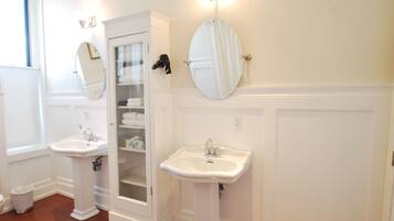 A bathroom with two white pedestal sinks, a glass-enclosed cabinet with towels, and wall-mounted mirrors.