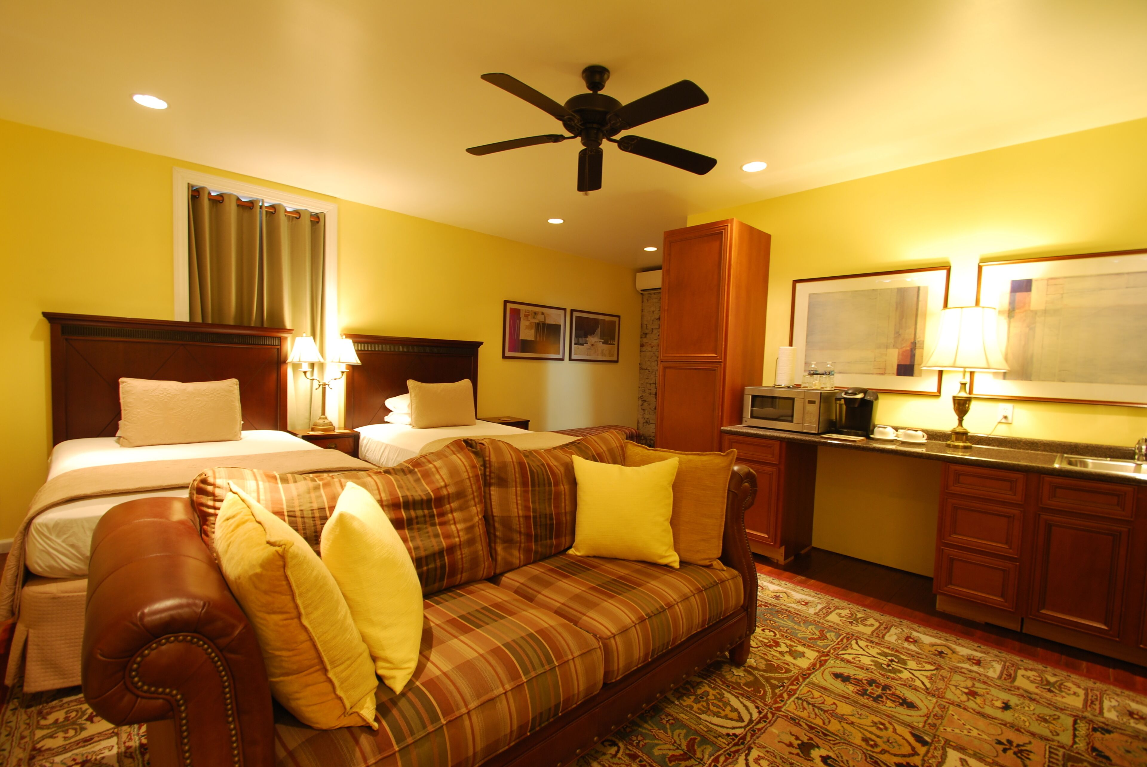 A hotel room with a bed, a sofa, a ceiling fan, a microwave, and a small kitchen area.