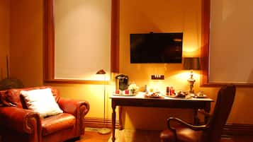 Una habitación acogedora con un sillón de cuero, un escritorio de madera con lámpara, cafetera y un televisor en la pared.