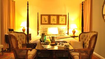A hotel room with a bed, two armchairs, a table with a lamp, and a bedside table with a lamp. There are framed pictures on the wall above the bed.