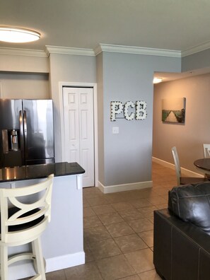 A kitchen with a refrigerator, a bar counter, and a door. There is a wall with the letters 'PCB' on it.