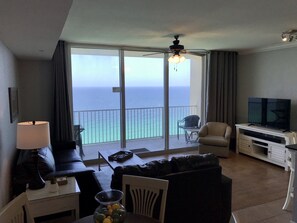 A hotel room with a balcony, a sofa, a television, and a dining table.