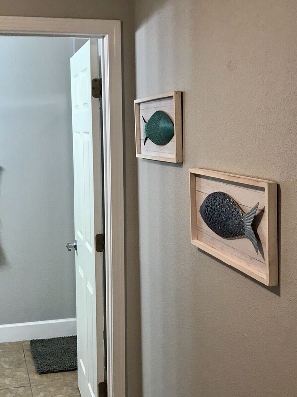 A hallway with a door leading to a room, a small rug, and two framed fish decorations on the wall.