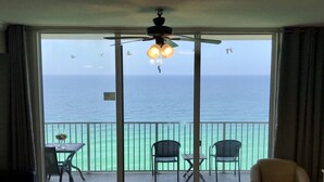 A room with a balcony overlooking the sea, featuring a ceiling fan, a table with chairs, and a sofa. - Beautiful gulf front, amazing views. Walk to Pier Park.   (Panama City Beach)