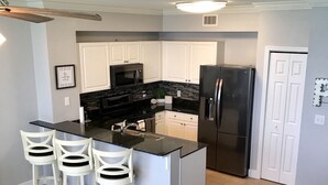A modern kitchen with white cabinets, a black refrigerator, and a bar area with three white bar stools. - Beautiful gulf front, amazing views. Walk to Pier Park.   (Panama City Beach)