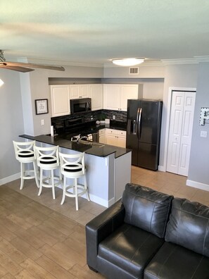 A modern kitchen with white cabinets, a black refrigerator, and a central island with bar stools.