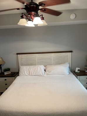 A bedroom with a bed, a nightstand, a lamp, and a ceiling fan.