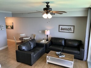 Un salon avec un canapé en cuir noir, une table basse blanche, un ventilateur de plafond et une lampe fixée au mur.