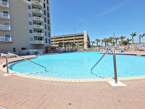 A swimming pool with a brick deck, surrounded by a multi-story building with balconies.