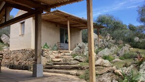 A rustic stone building with a wooden pergola, a stone staircase, and a view of the surrounding rocky landscape.