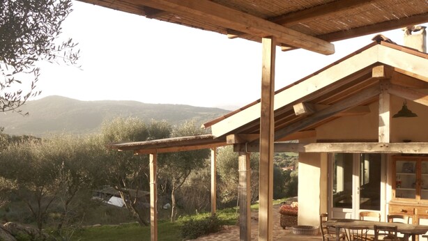 A rustic wooden structure with a stone floor, a dining area with a table and chairs, and a view of a mountainous landscape.