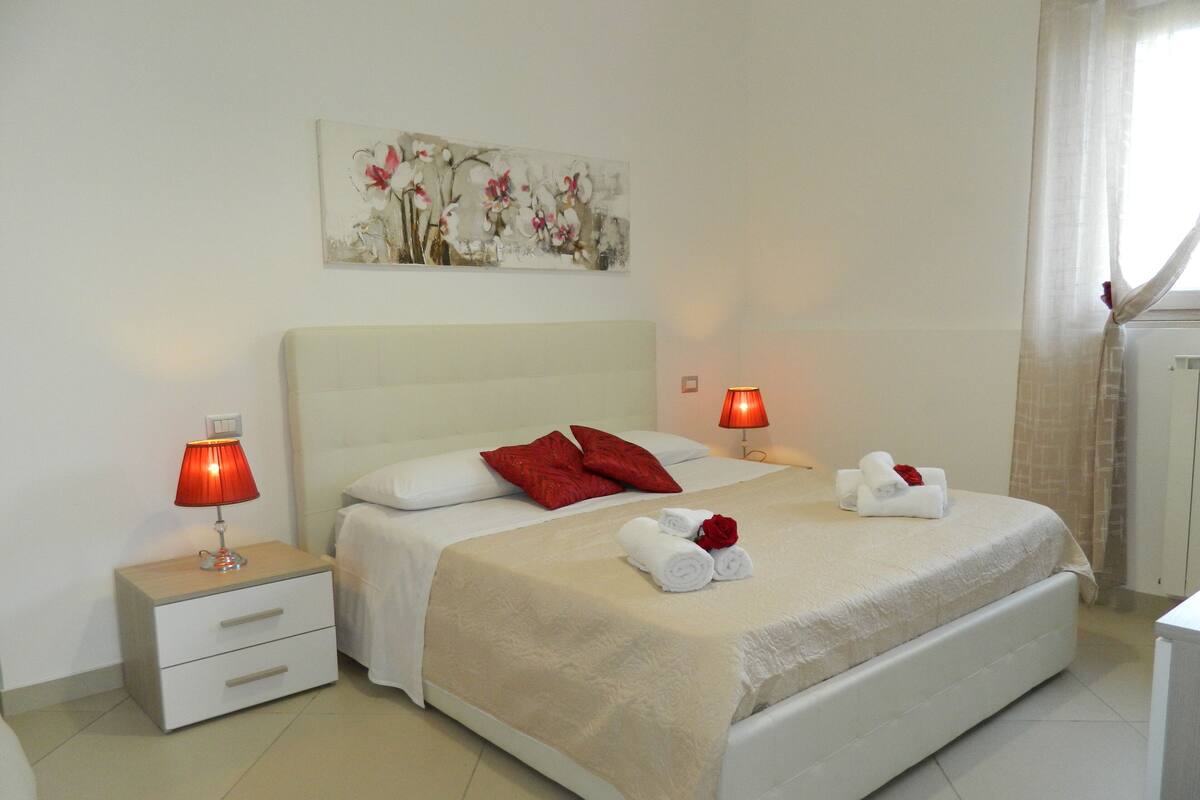 A hotel room with a large bed, two bedside tables with lamps, a painting on the wall, and a window with curtains.