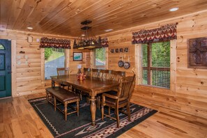 A wooden cabin interior with a dining table, benches, and a chandelier.