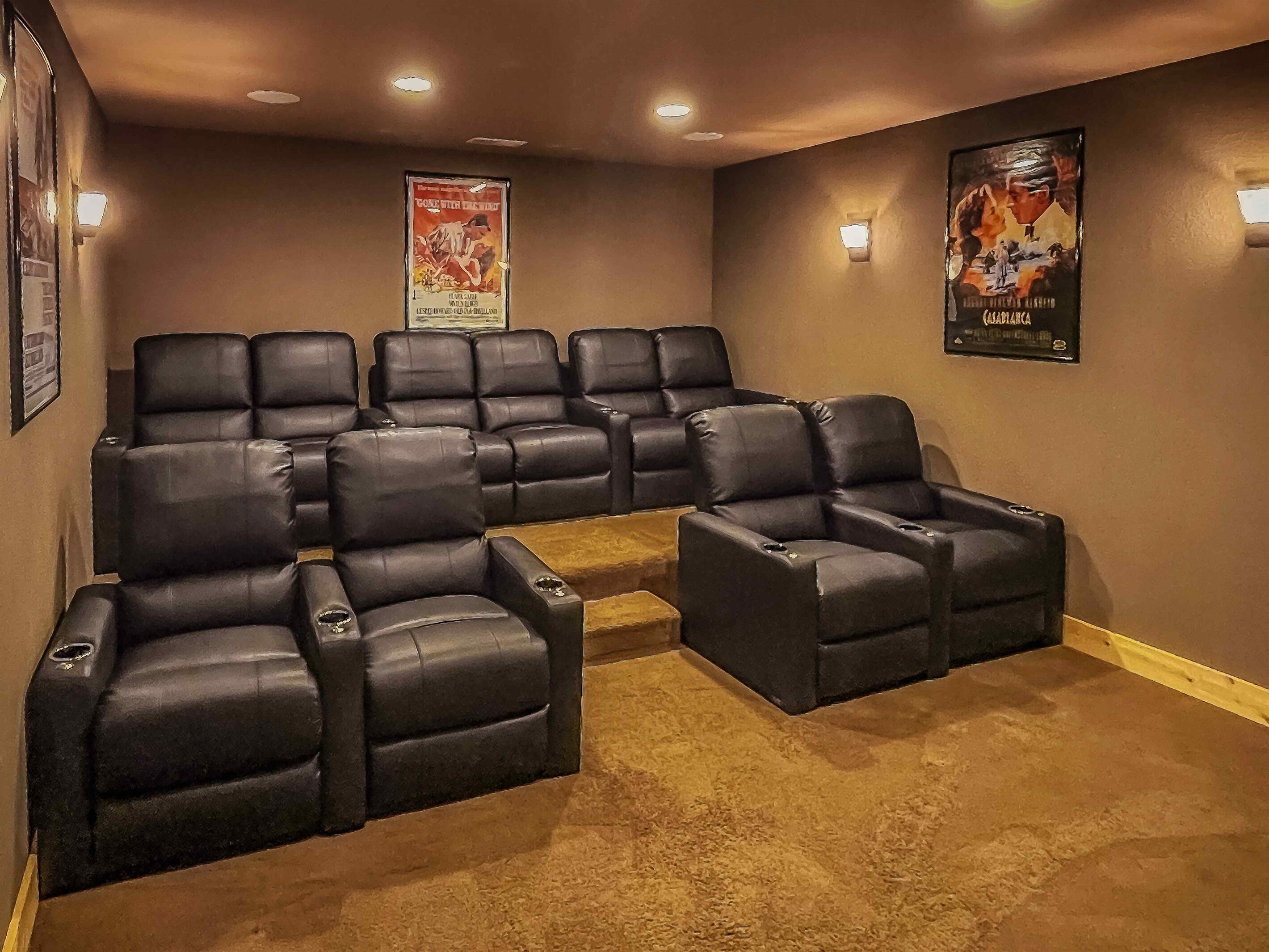 A home theater room with a sectional sofa and a recliner, carpeted floor, and posters on the walls.