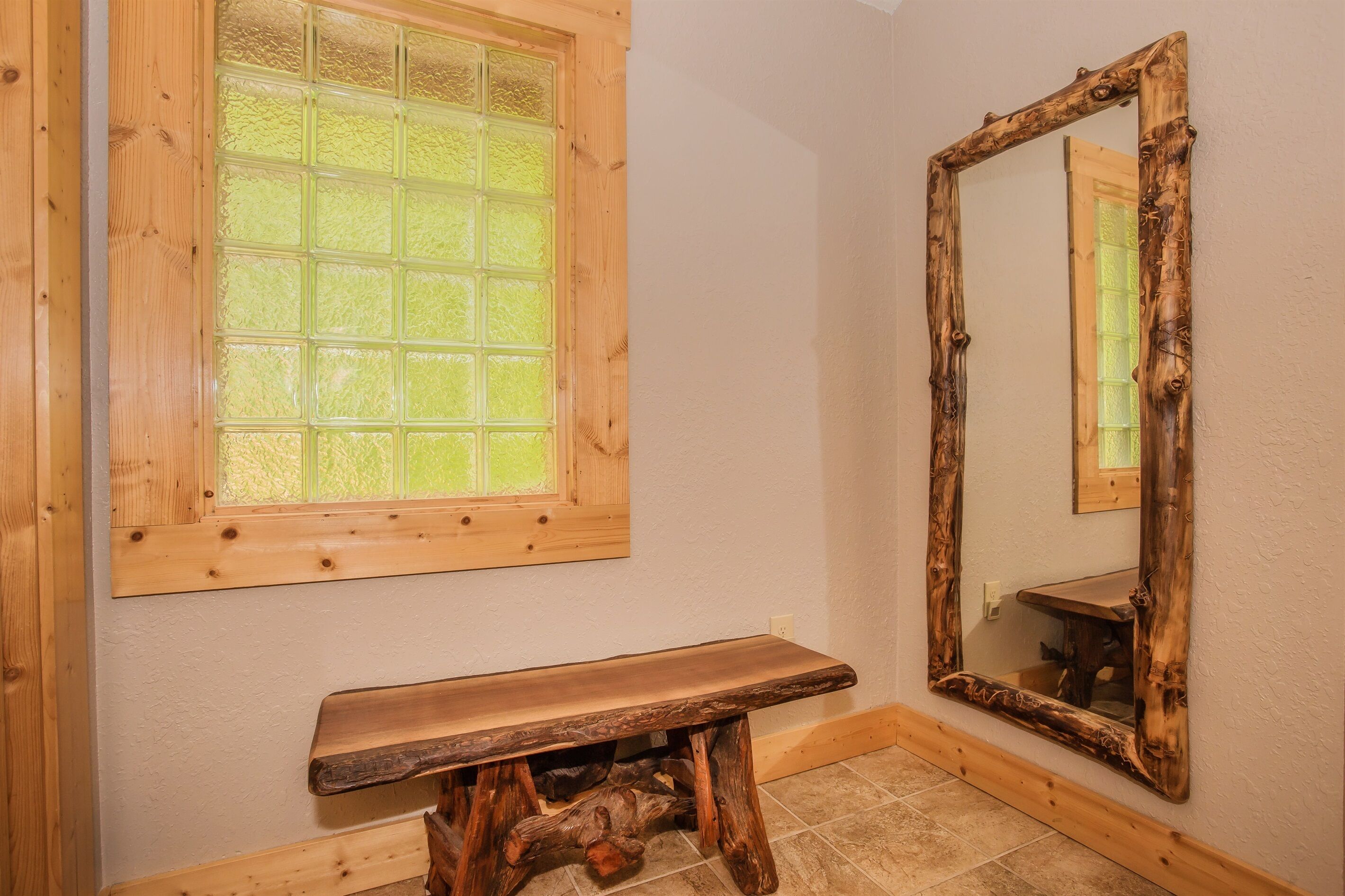 A bathroom with a wooden bench, a window with frosted glass, and a mirror with a rustic frame.