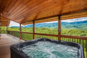 A hot tub on a wooden deck with a view of a forested mountain range.