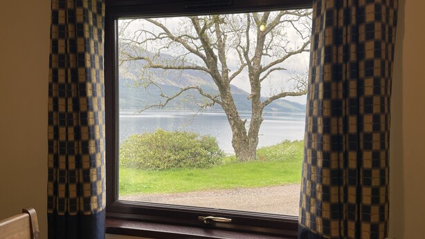 Ein Zimmer mit großem Fenster und Blick auf einen See und Berge.