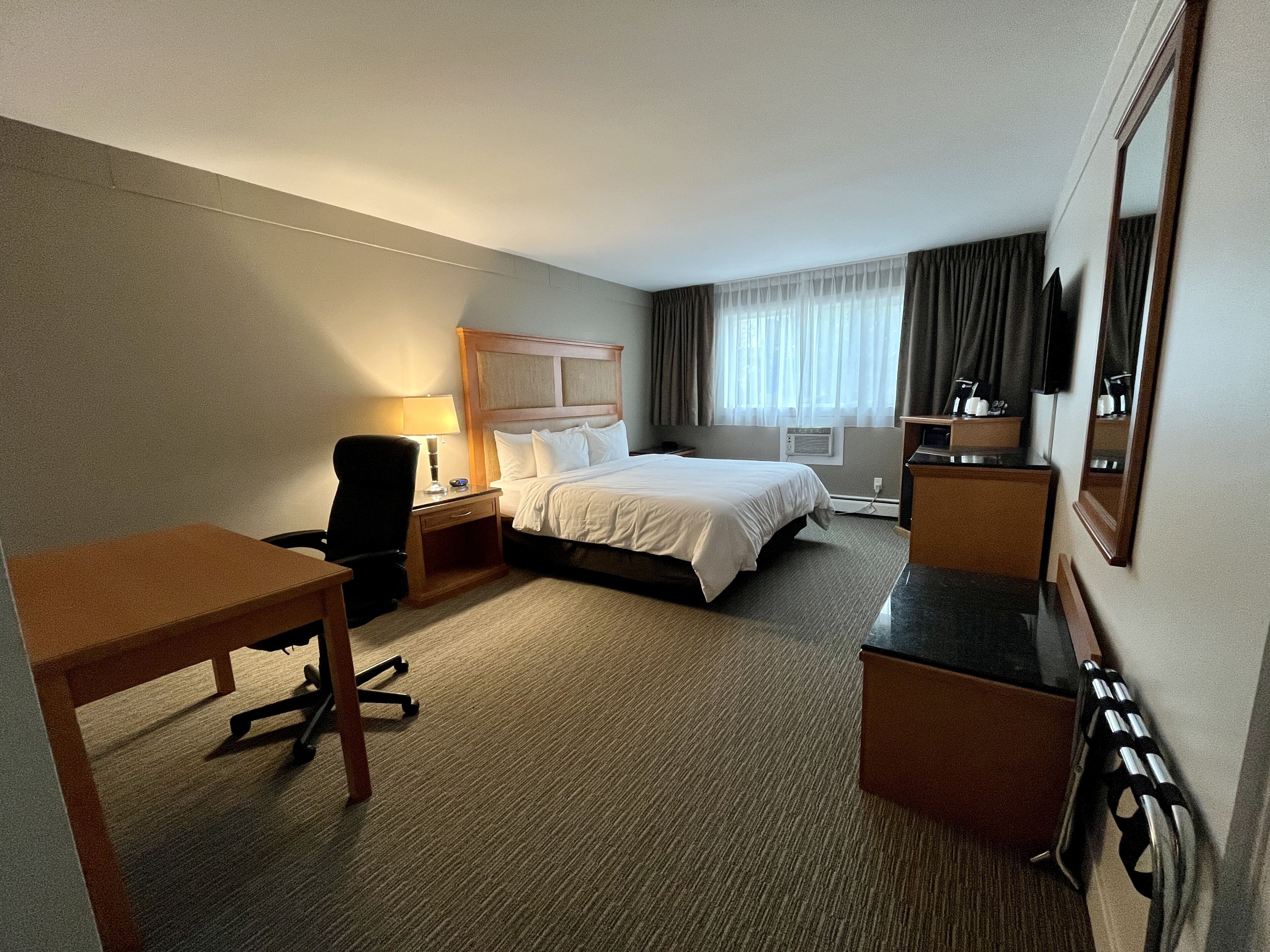 A hotel room with a bed, desk, chair, and a TV.